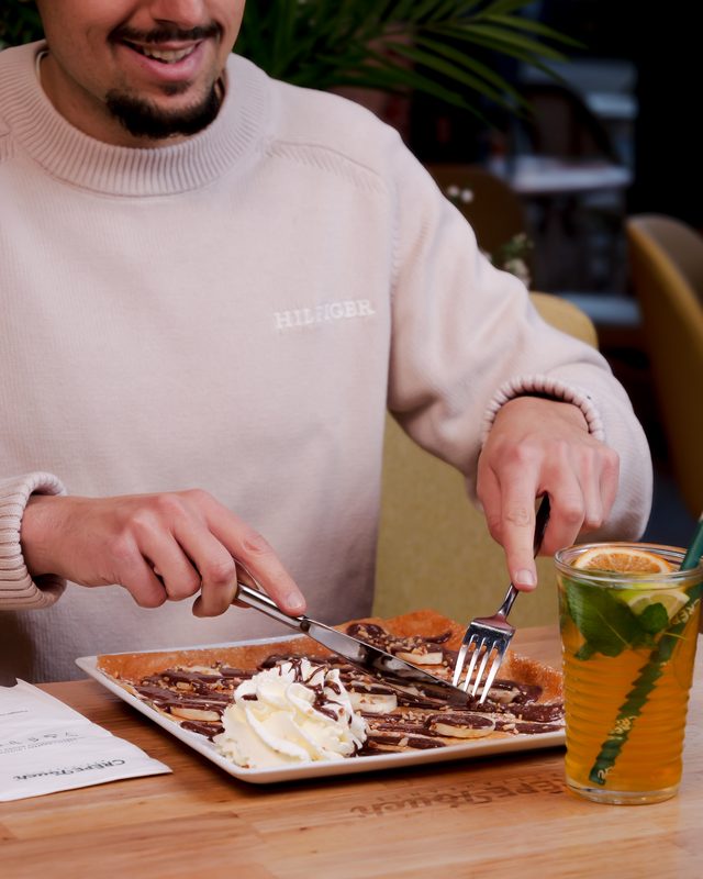 Client souriant dégustant une crêpe chocolat avec boisson fraîche